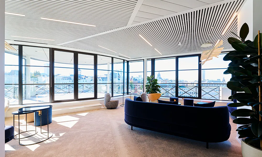 Corner office lounge with curved navy sofa, designer chairs and panoramic city views