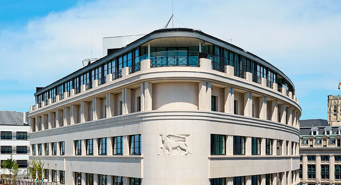 Modern curved limestone office building with glass upper floors under a clear blue sky