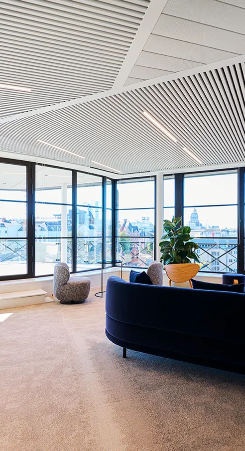 Top-floor office lounge with a navy sofa, armchairs and floor-to-ceiling windows overlooking the city