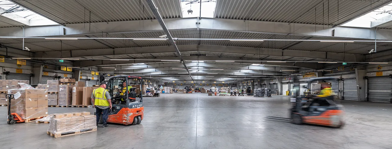 Interior of a distribution warehouse with forklifts moving pallets between storage bays