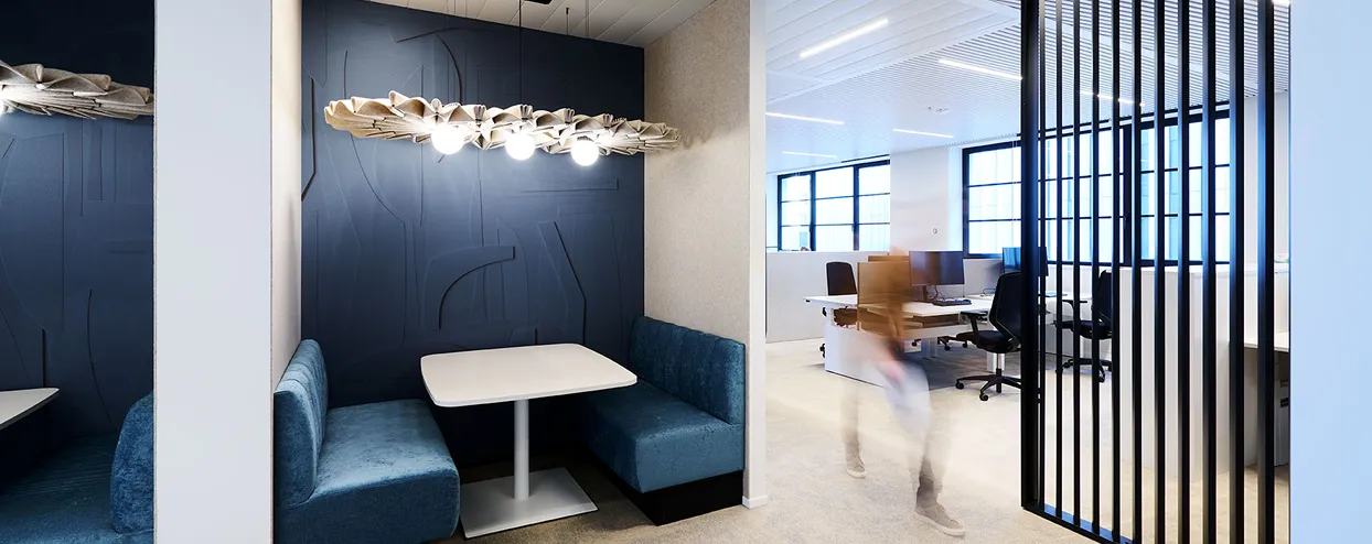 Quiet office booth with blue upholstered benches beside an open workspace area